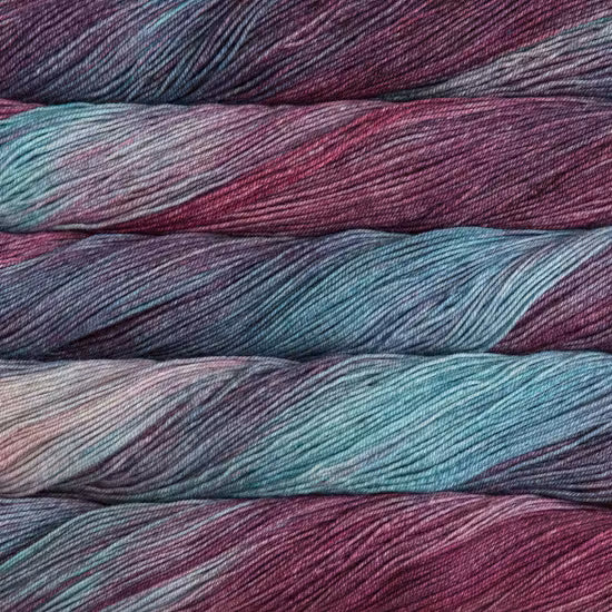 Close-up of variegated yarn skeins showing a color-shifting pattern of teal blue, plum purple, and dusty rose.