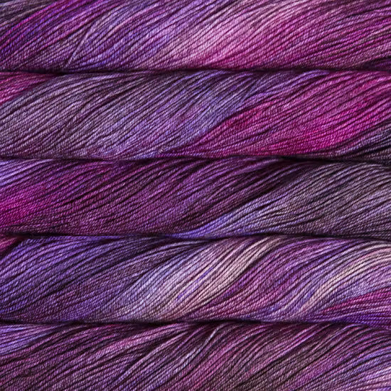 Close-up of folded yarn strands showing a variegated colorway of deep purple, magenta, and violet.