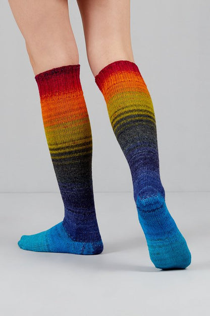 Knitted socks in deep blue, purple, red, orange, and yellow tones from Urth Yarns in the Gusto line