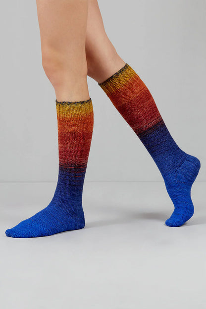 Knitted socks in blue, red, and yellow tones from Urth Yarns in the Gusto line