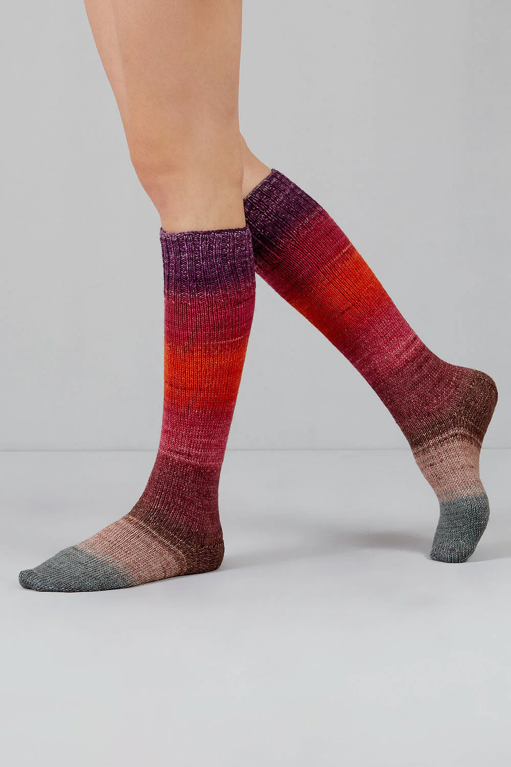 Knitted socks in grey, red, pink, purple, and brown tones from Urth Yarns in the Gusto line