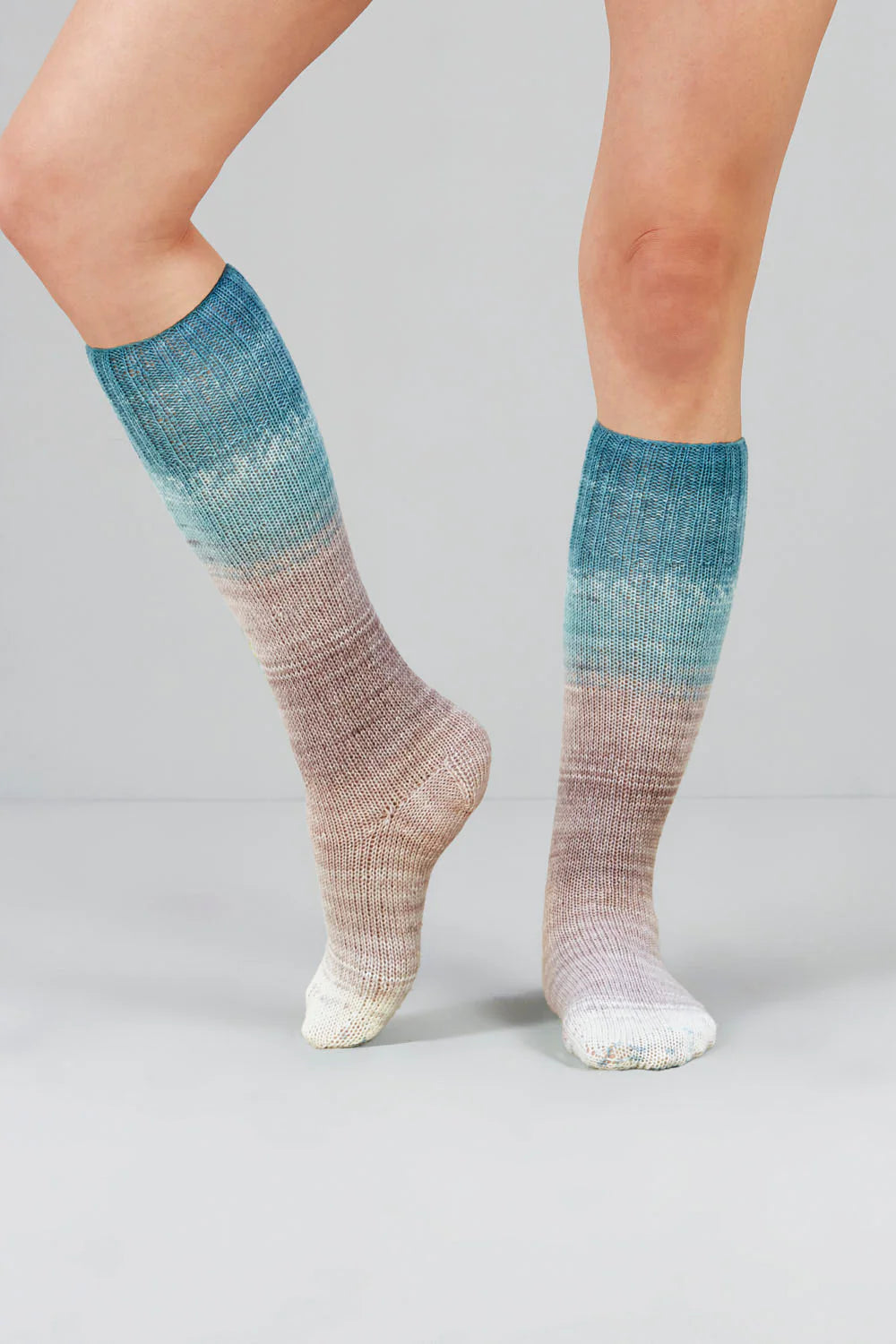 Knitted socks in light blue, grey, and white tones from Urth Yarns in the Gusto line