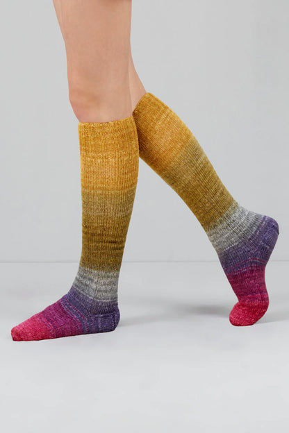 Knitted socks in pink, purple, grey, and golden tones from Urth Yarns in the Gusto line