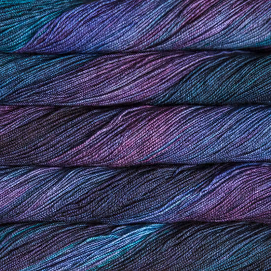 Close-up of folded yarn strands showing a variegated color pattern of deep purple, blue, and teal.