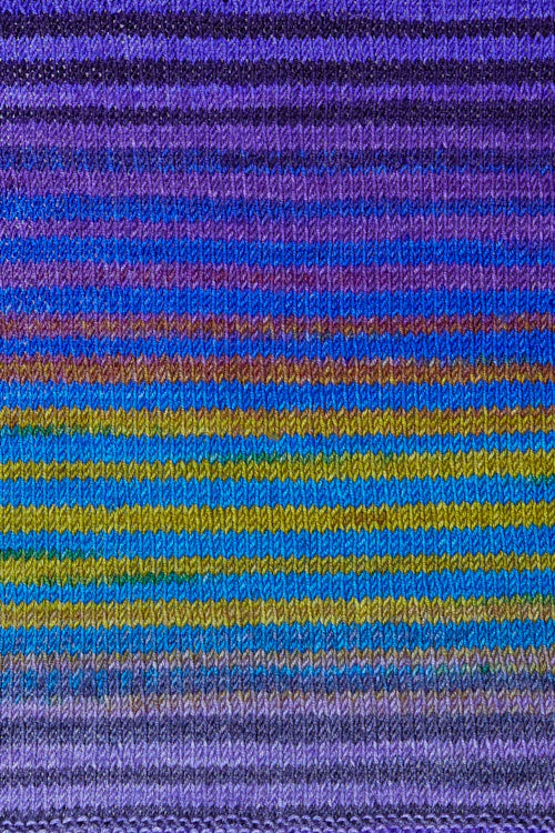 a knitted swatch of merino yarn with purple, green, and blue tones from Urth yarns