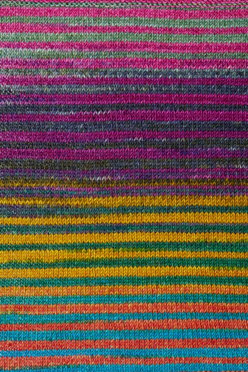 a knitted swatch of merino yarn with pink, yellow, grey, orange, and teal tones from Urth yarns