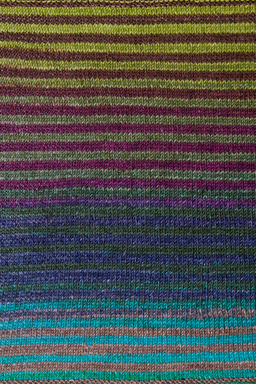 a knitted swatch of merino yarn with green, grey, purple, and blue tones from Urth yarns
