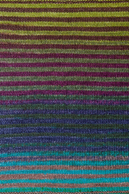 a knitted swatch of merino yarn with green, grey, purple, and blue tones from Urth yarns