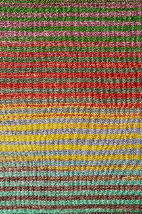 a knitted swatch of merino yarn with yellow, green, red, grey, and teel tones from Urth yarns