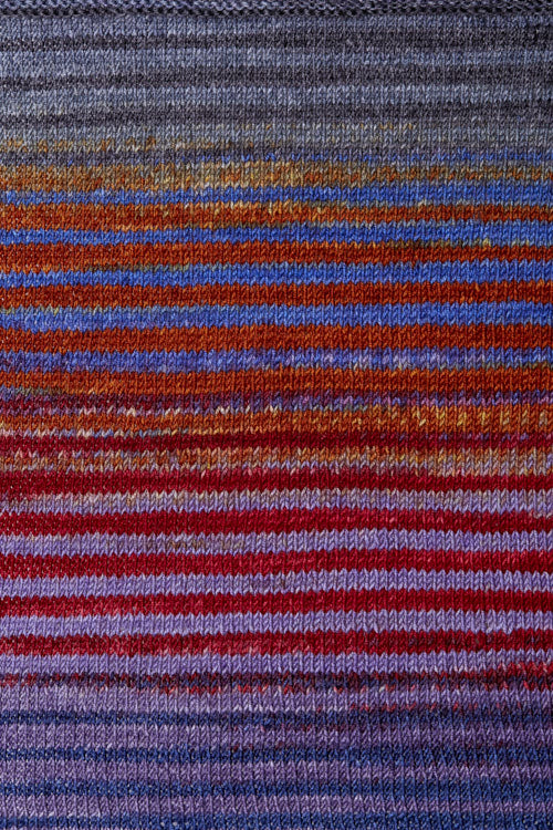 a knitted swatch of merino yarn with purple, red, and orange tones from Urth yarns