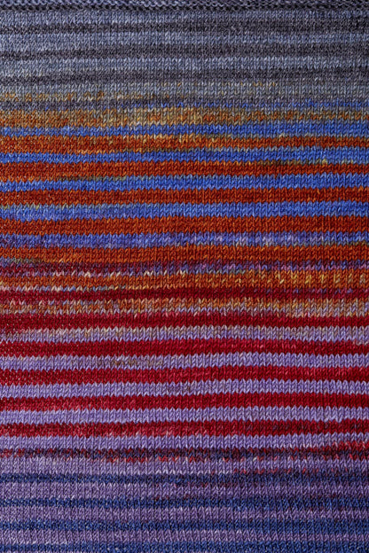 a knitted swatch of merino yarn with purple, red, and orange tones from Urth yarns