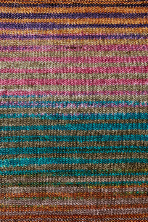 a knitted swatch of merino yarn with purple, orange, pink and teal tones from Urth yarns