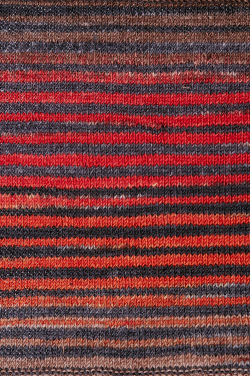 a knitted swatch of merino yarn with red, grey, and orange tones from Urth yarns
