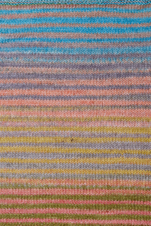 a knitted swatch of merino yarn with teal, grey, green, and peach tones from Urth yarns