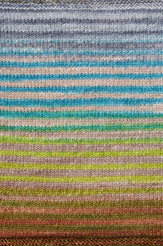 a knitted swatch of merino yarn with blue, grey, green, and grey tones from Urth yarns