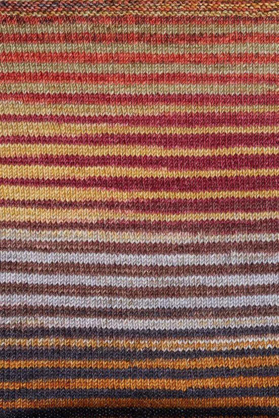 a knitted swatch of merino yarn with orange, yellow, brown, and grey tones from Urth yarns
