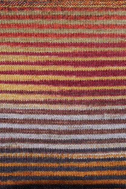 a knitted swatch of merino yarn with orange, yellow, brown, and grey tones from Urth yarns