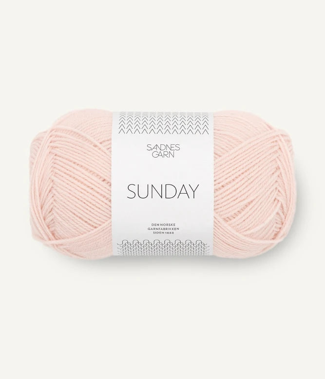 A ball of Sandnesgarn Sunday merino wool yarn in a blush color, with packaging that includes the brand and product name.