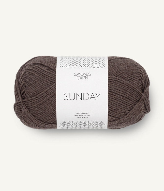 A ball of Sandnesgarn Sunday merino wool yarn in a dark brown color, with packaging that includes the brand and product name.