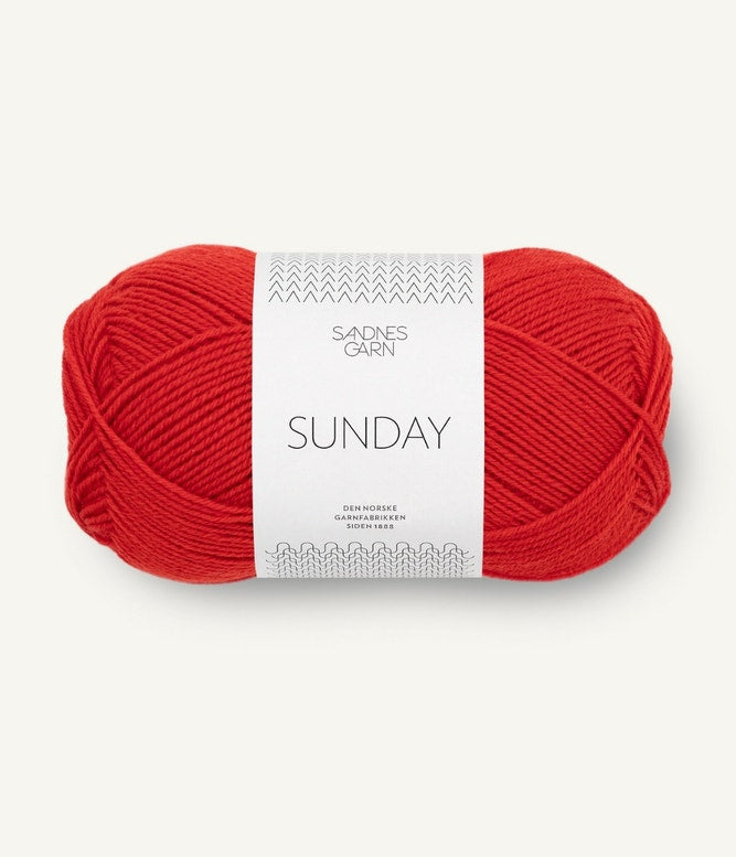 A ball of Sandnesgarn Sunday merino wool yarn in a red color, with packaging that includes the brand and product name.
