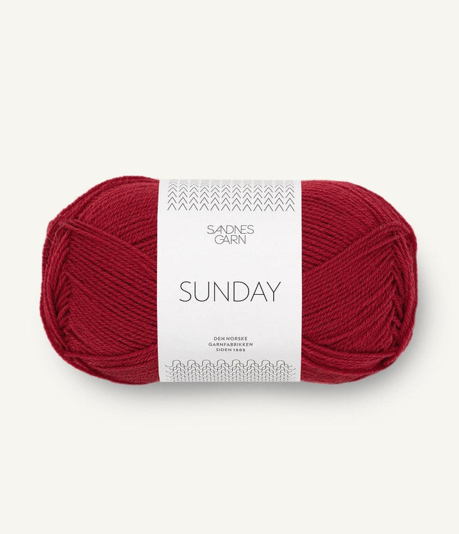 A ball of Sandnesgarn Sunday merino wool yarn in a deep red color, with packaging that includes the brand and product name.