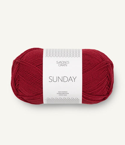 A ball of Sandnesgarn Sunday merino wool yarn in a deep red color, with packaging that includes the brand and product name.