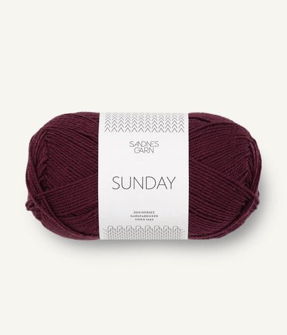 A ball of Sandnesgarn Sunday merino wool yarn in a plum color, with packaging that includes the brand and product name.