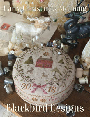 A cross stitch chart depicting a festive scene with Christmas-themed elements, such as trees and ornaments, and the text 'Blackbird Designs' at the bottom.
