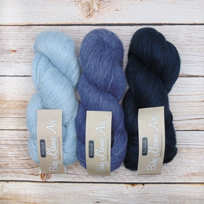 Three skeins of yarn in blue and navy labeled 'Baby Llama Air' by Estelle. 