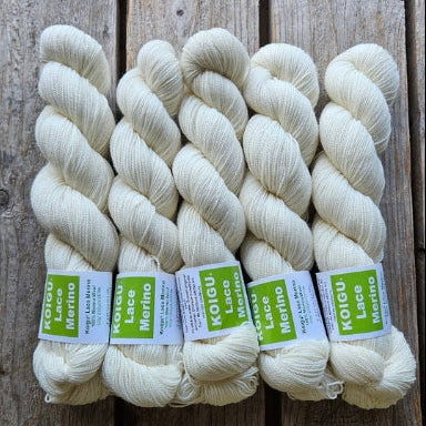Four skeins of white colored merino lace weight yarn labeled 'Koigu Lace Merino'. 
