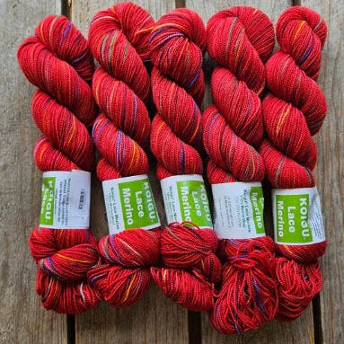 Four skeins of red colored merino lace weight yarn labeled 'Koigu Lace Merino'. 