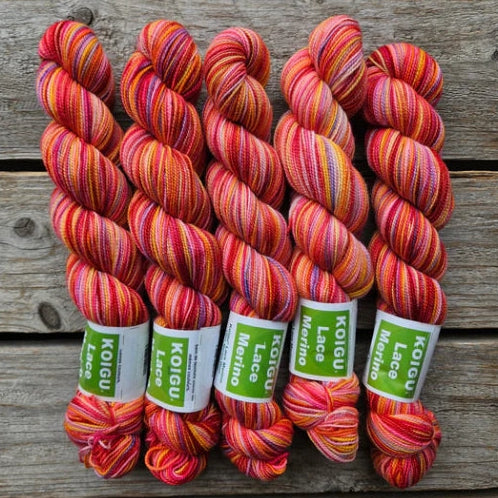 Four skeins of variegated red and pink colored merino lace weight yarn labeled 'Koigu Lace Merino'. 