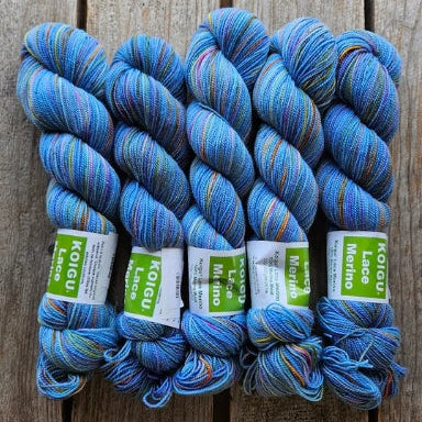 Four skeins of blue variegated colored merino lace weight yarn labeled 'Koigu Lace Merino'. 