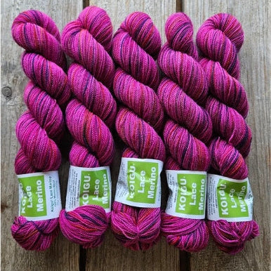 Four skeins of magenta colored merino lace weight yarn labeled 'Koigu Lace Merino'. 