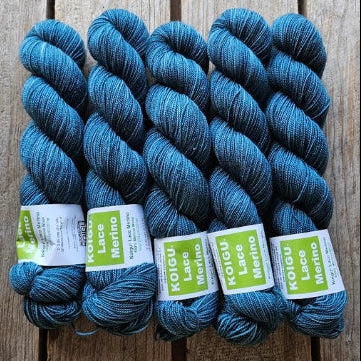 Four skeins of blue colored merino lace weight yarn labeled 'Koigu Lace Merino'. 
