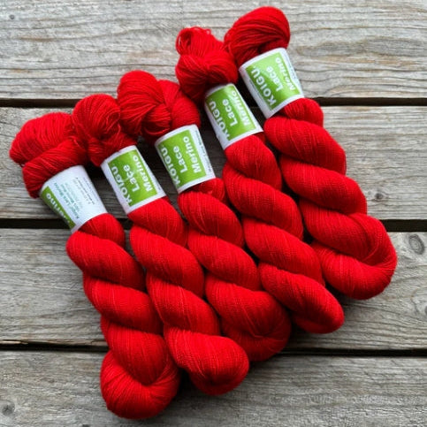 Four skeins of red colored merino lace weight yarn labeled 'Koigu Lace Merino'. 