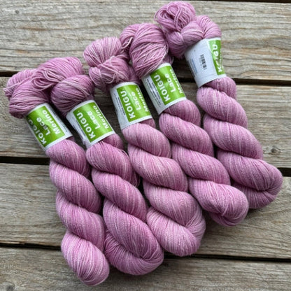 Four skeins of pink colored merino lace weight yarn labeled 'Koigu Lace Merino'. 