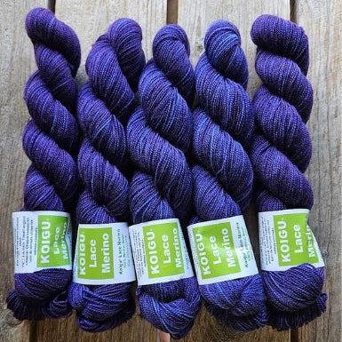Four skeins of purple colored merino lace weight yarn labeled 'Koigu Lace Merino'. 