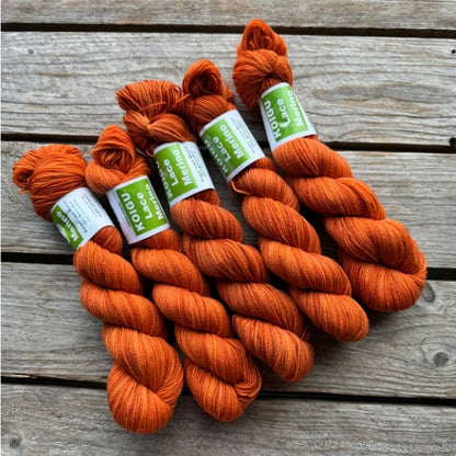 Four skeins of orange colored merino lace weight yarn labeled 'Koigu Lace Merino'. 