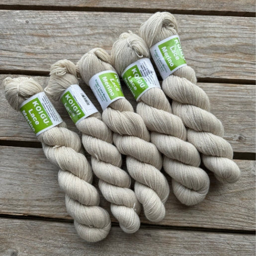 Four skeins of off-white colored merino lace weight yarn labeled 'Koigu Lace Merino'. 