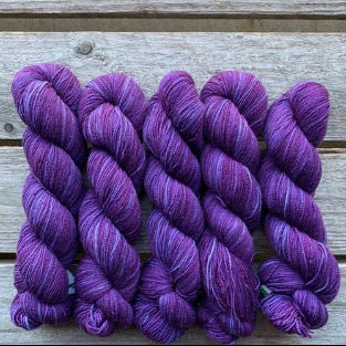 Four skeins of purple colored merino lace weight yarn labeled 'Koigu Lace Merino'. 