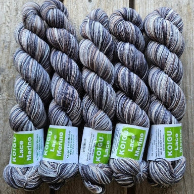 Four skeins of variegated grey colored merino lace weight yarn labeled 'Koigu Lace Merino'. 