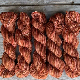 Four skeins of orange colored merino lace weight yarn labeled 'Koigu Lace Merino'. 