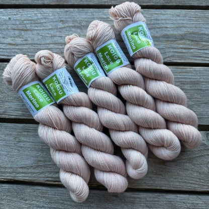 Four skeins of off-white colored merino lace weight yarn labeled 'Koigu Lace Merino'. 