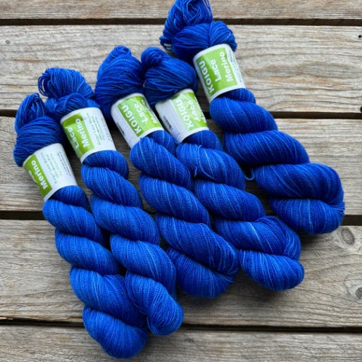 Four skeins of blue colored merino lace weight yarn labeled 'Koigu Lace Merino'. 