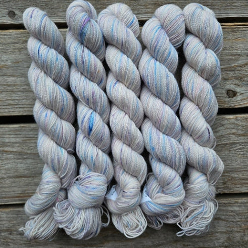 Four skeins of white and blue colored merino lace weight yarn labeled 'Koigu Lace Merino'. 