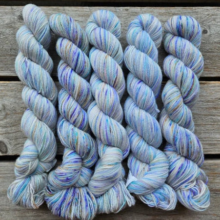 Four skeins of white and blue colored merino lace weight yarn labeled 'Koigu Lace Merino'. 