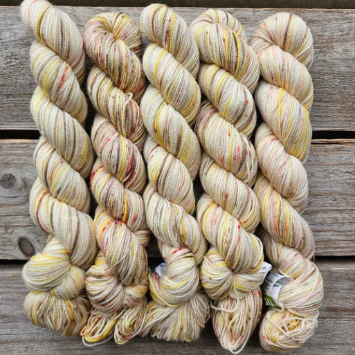 Four skeins of variegated beige colored merino lace weight yarn labeled 'Koigu Lace Merino'. 