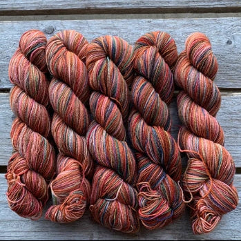 Four skeins of rust colored merino lace weight yarn labeled 'Koigu Lace Merino'. 