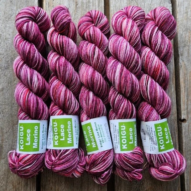 Four skeins of pink colored merino lace weight yarn labeled 'Koigu Lace Merino'. 